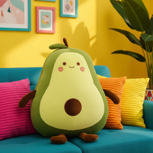 Avocado-shaped plush toy on a colorful couch with a yellow wall and framed pictures in the background.