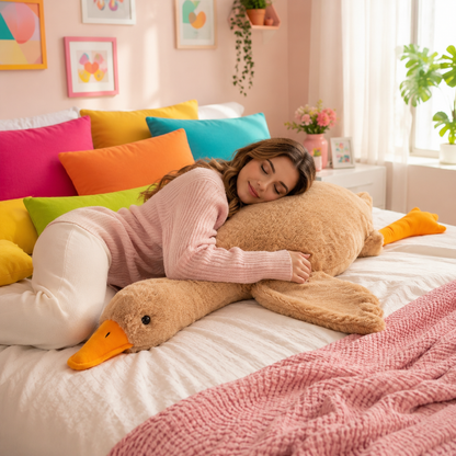 A woman in a pink ribbed sweater and white pants rests on a bed with a large plush goose pillow. The room has pastel pink walls, colorful pillows, framed art, and a bright window with plants.