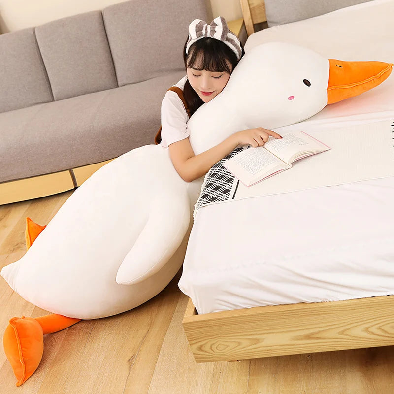 Person lying on a bed with a large goose shaped plushie body pillow