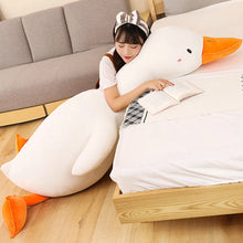 Person lying on a bed with a large goose shaped plushie body pillow