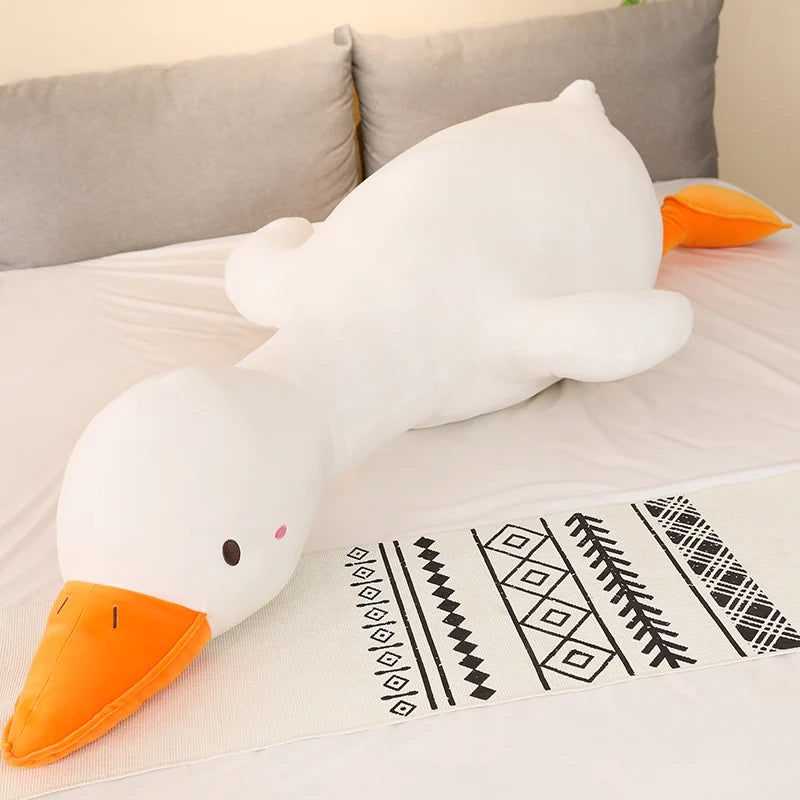 Large white goose-shaped plushie pillow with an orange beak on a couch.