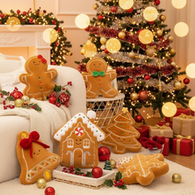 Decorative plushie gingerbread cookies and a house on a table with a Christmas tree and lights in the background.