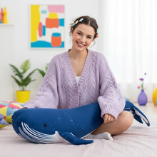 Woman holding a blue plush whale toy in a room with colorful abstract art on the wall.