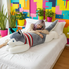 Person lying on a bed with a large dog-shaped pillow against a colorful wall.