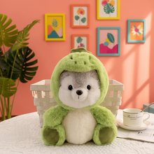 Plush toy in a green hood sitting on a table with a colorful wall and plant in the background