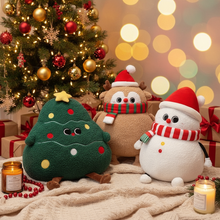 Three Christmas-themed plush toys in front of a decorated tree with lights and presents.