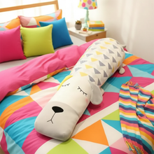 Colorful bedding set with a long pillow shaped like a dog on a bed.