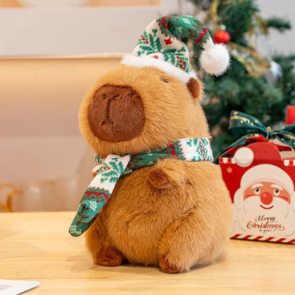 Plush capybara toy with Christmas hat and scarf in front of a decorated Christmas tree.