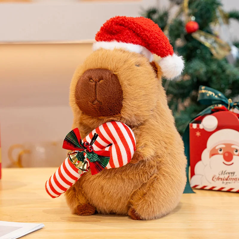 Capybara plushie wearing a Santa hat and striped candy cane with a Christmas tree in the background