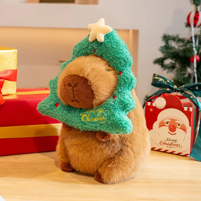 Capybara plush toy in a Christmas tree costume with presents and a Santa Claus box in the background.