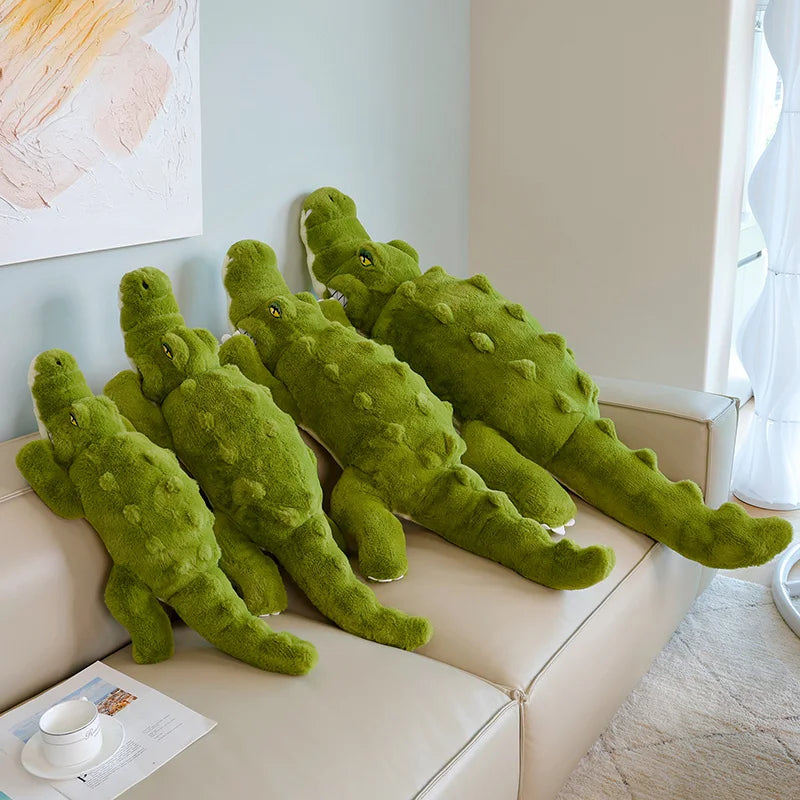Green plush alligator body pillows on a beige couch in a room with light-colored walls.