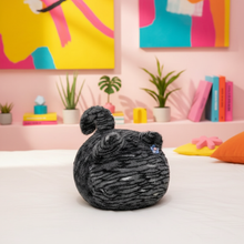 Black plush cat on a bed with colorful wall art and decor in the background