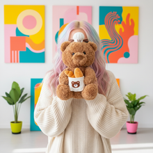 Person holding a teddy bear with a baker design in a room with colorful abstract paintings.
