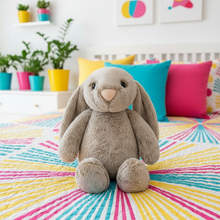 Gray plush bunny toy on a colorful bedspread with a room in the background