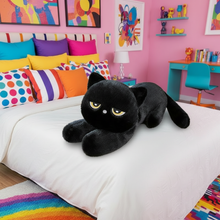 Black plush cat toy on a bed in a colorful bedroom with pillows and artwork.