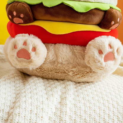 Plush toy shaped like a hamburger with paw-like paws on a textured surface