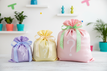 Three gift bags with question marks in pastel colors on a white surface.