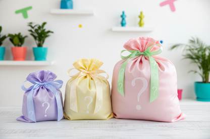 Three gift bags with question marks in pastel colors on a white surface.