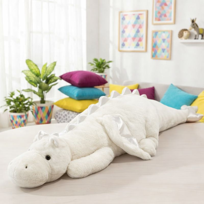 Large white dragon plush toy on a couch in a bright living room with colorful pillows and plants.
