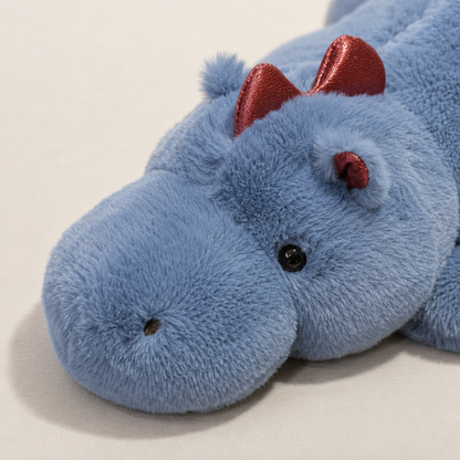 A close-up of a blue plush dragon toy with shiny red ears and small black eyes, lying on a light beige surface.