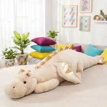 Large plush dragon toy on a sofa in a bright living room with colorful pillows and plants.
