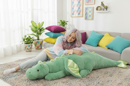 Woman lying on a large green dragon-shaped pillow in a living room with colorful pillows and plants.
