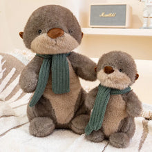 Two plush otters wearing green scarves on a soft surface.