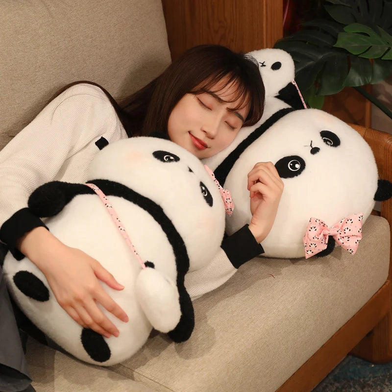 Person holding two panda-shaped pillows with a bow on a couch