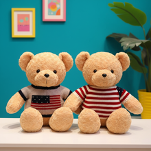 Two teddy bears wearing American-themed sweaters on a white surface with a blue wall and plant in the background.