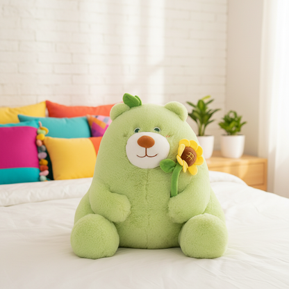 Green teddy bear with a sunflower on a bed with colorful pillows and plants in the background