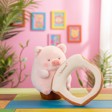 Plush pig toy with a bread-shaped plush on a colorful floor with a pink wall and framed pictures in the background.