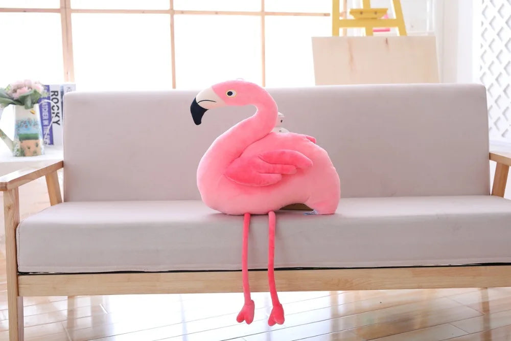 Pink flamingo plush toy on a light gray sofa in a room with a window and decor.
