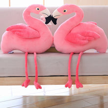 Two pink flamingo plush toys sitting on a white surface.