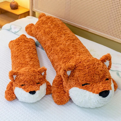 Two kawaii plushie body pillow fox toys on a bed with a wooden nightstand in the background.