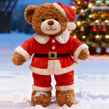 Teddy bear in a Santa Claus outfit standing in the snow with a Christmas tree in the background.