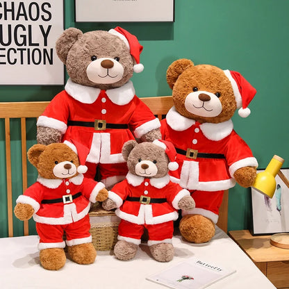 Set of teddy bears dressed in Santa Claus outfits on a bed with a green wall in the background.