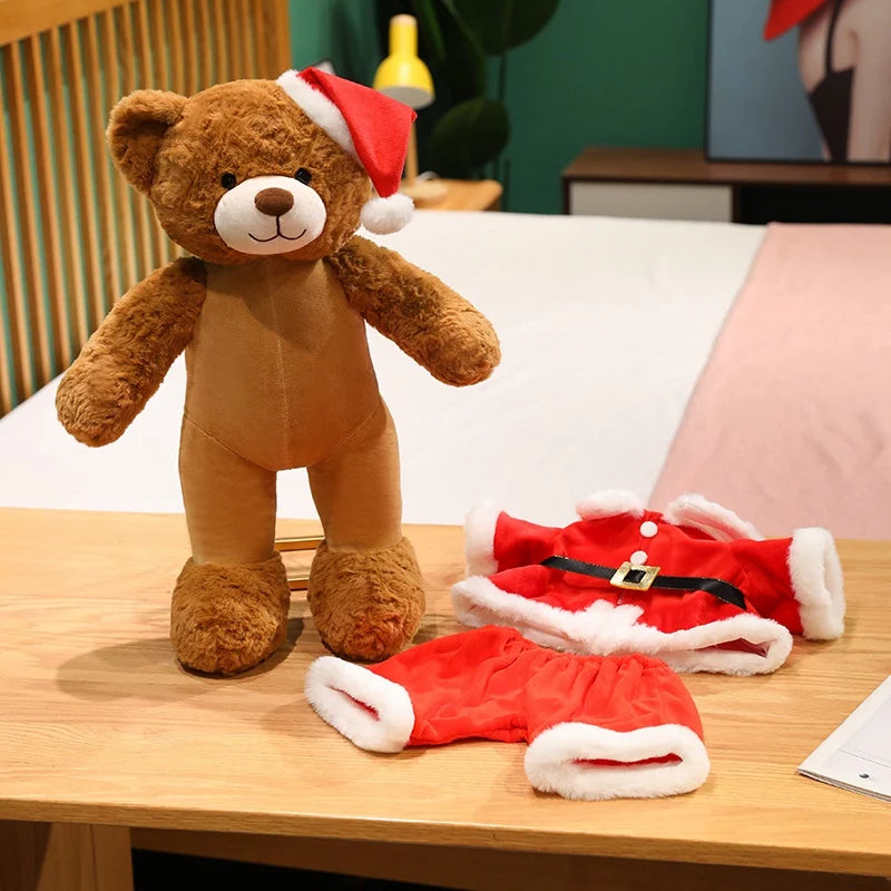 Brown teddy bear wearing a Santa hat with a red outfit on a wooden table.
