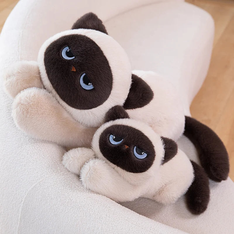 Two Siamese cat plush toys sitting on a white cushion.