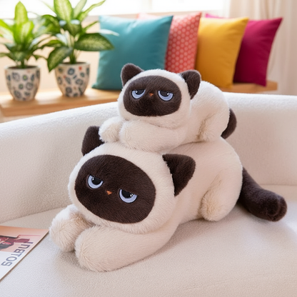 Two plush cat toys stacked on a couch with colorful pillows and plants in the background.
