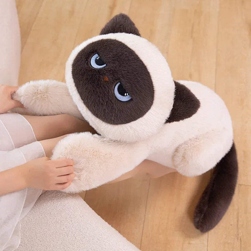 Person holding a large Siamese cat plush toy on a wooden floor
