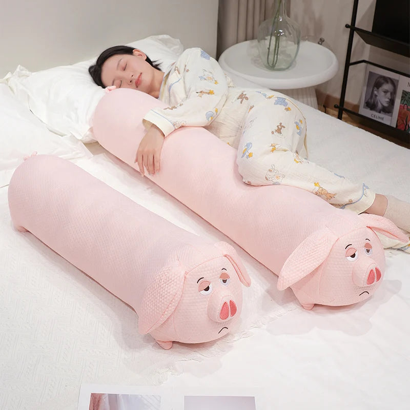 Person lying on a bed with a pink pig-shaped body pillow and headrest.