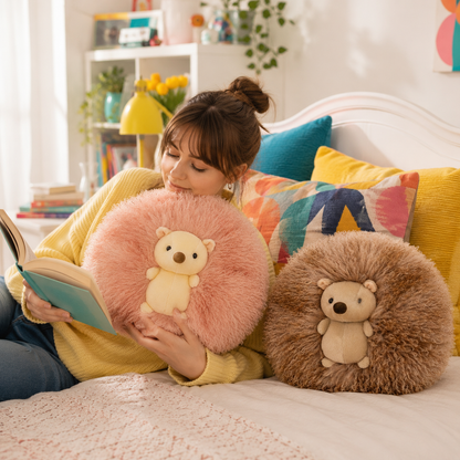 A cozy bedroom scene with a woman reading a book while lying on a bed, surrounded by two round plush hedgehog pillows. One pillow is light pink with a cream bear face, and the other is brown with a cream bear face.