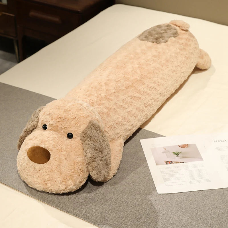 Long dog-shaped plushie body pillow on a bed with a magazine underneath