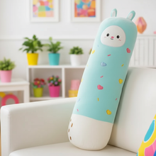 Cylindrical plush toy with cartoon face on a white couch in a bright room with plants and colorful decor.