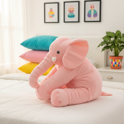 Pink elephant plush toy on a bed with colorful pillows and a plant in the background.