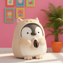 Plush toy penguin in a beige hood with a pink wall and plant in the background