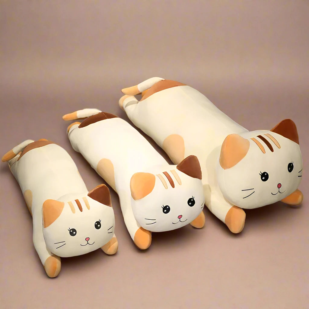 Set of cat-shaped plush toys on a bed with a lamp and wall art in the background.