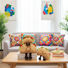 Three plush taco toys on a coffee table with colorful pillows and abstract wall art in the background.