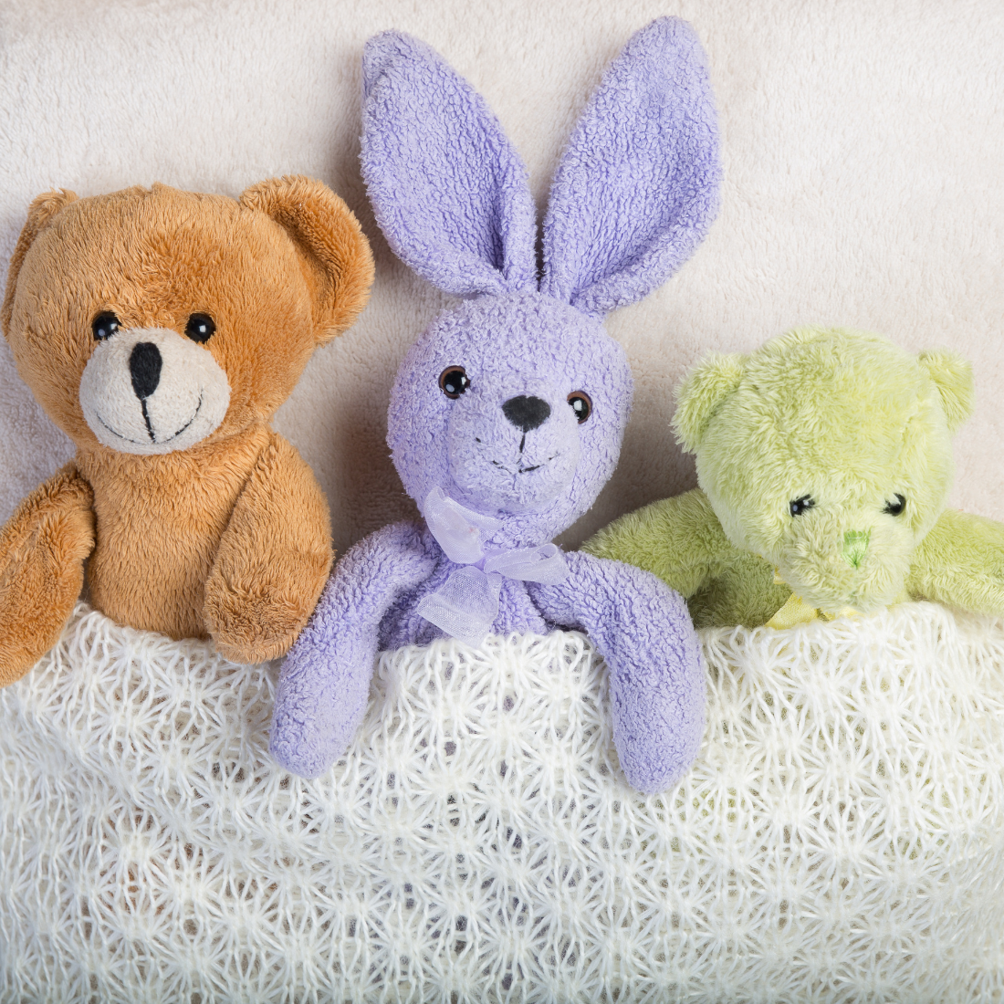 Three plush toys, rabbit and two bears, tucked into a bed.