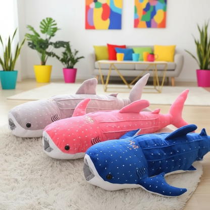 Three colorful whale shark-shaped plush toys on a light-colored rug with a modern living room in the background.